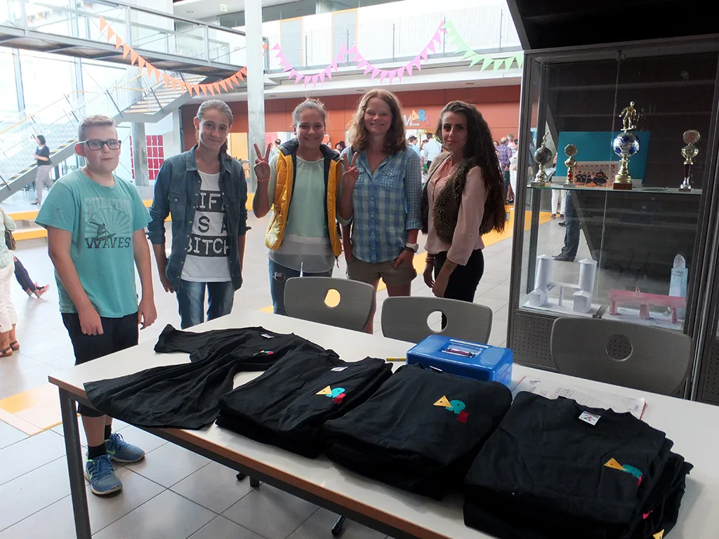 Jugendliche stehen an einem Tisch mit Schul-T-Shirts.